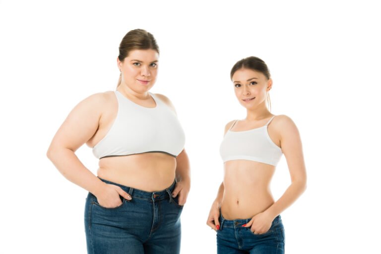 smiling overweight and slim women posing with hands in pockets isolated on white, body positivity